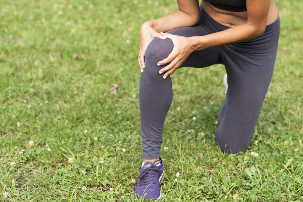 Knee pain symptom shown by person holding knee, sports therapy Sacramento for injury relief.